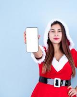 primer plano de una mujer feliz caucásica con ropa de santa apuntando al teléfono inteligente foto