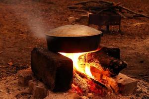 cocinar comida en una sartén de hierro fundido en una hoguera cerca del campamento por la noche. foto