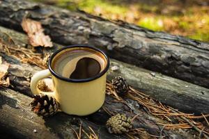 taza de metal amarillo con café caliente en el fondo de madera con monedas, agujas y corteza de árbol. foto
