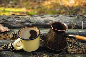 Yellow metal  cup with hot coffee and cezve on the wooden background with the coins, needles and bark of tree. photo