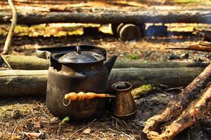 tetera de metal negro y cezve sobre el fondo de madera en el bosque de coníferas. foto