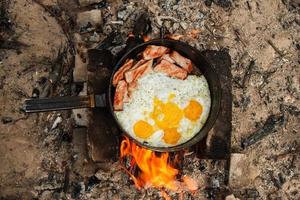 Scrambled eggs with bacon on the cast-iron pan on a bonfire, top view. photo