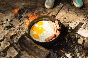 Scrambled eggs with bacon on the cast-iron pan on a bonfire, top view. photo