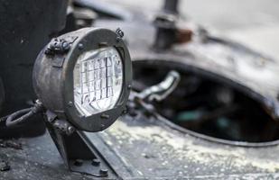 Front headlight of a Soviet battle tank. Very bright searchlight on the tank turret, close-up. Armored infantry fighting vehicle. Fragment of an old armored personnel carrier, khaki headlight. photo