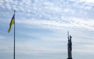 The Ukrainian flag fluttering in the wind against the blue sky, near the famous statue of the Motherland. Famous sights, monuments and monuments of Kyiv. Ukraine, Kyiv - October 08, 2022. photo