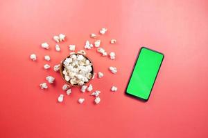 top view of smart phone and popcorn on red background photo