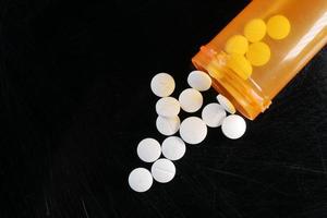 white color medical pills spilling from a orange color container on black photo