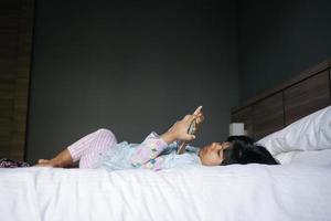 Child girl watching cartoon on smart phone lying on bed photo