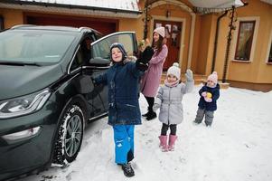 Young woman with kids hold eco bags and charging electric car in the yard of her house . photo