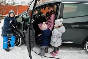 Young mother with kids charging electric car in the yard of her house at winter. photo