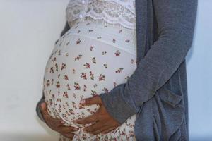 Pregnant woman caressing her belly and making a heart shaped gesture with her fingers signifying her love for her unborn child. photo