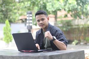 Atractivo joven asiático usando una laptop en un espacio de trabajo conjunto con cara feliz foto