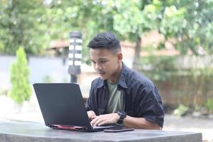 Atractivo joven asiático usando una laptop en un espacio de trabajo conjunto con cara feliz foto