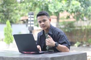 Attractive young Asian man using laptop in co-working space with happy face photo