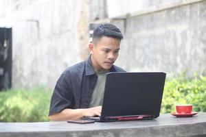 Atractivo joven asiático usando una laptop en un espacio de trabajo conjunto con cara feliz foto