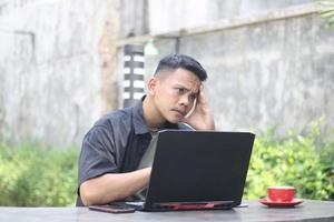 Attractive young Asian man using laptop confused in co-working space with unhappy face photo