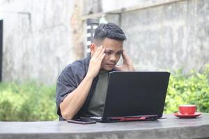 Attractive young Asian man using laptop confused in co-working space with unhappy face photo