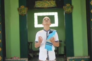 Young asian muslim praying in the mosque carrying a prayer mat photo