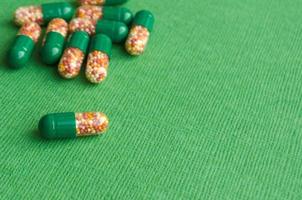 Green pills. Transparent colorful pills on a green background. Capsules with granules. Copy space for text. Treatment concept. photo