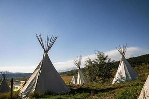 View of teepees on grassy field with blue sky in background during summer photo