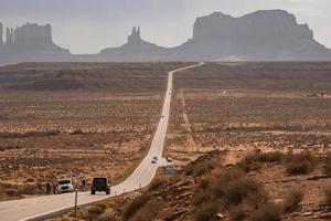 Cars on road amidst landscape leading towards Monument Valley during summer photo