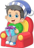 The happy boy is sitting on the sofa and holding the big santa gift vector