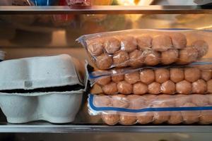 lot of sausages lie on a glass shelf inside a home refrigerator photo