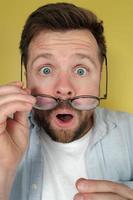 Man with a shocked expression holds his glasses, which he took off in surprise. Close-up. photo