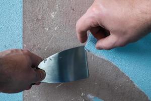Hand removes old blue wallpaper from the walls, using a spatula. House renovation. photo