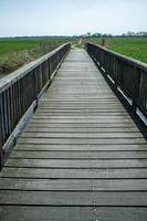 Pedestrian bridge passes over a moat filled with water, against the backdrop of fields. photo