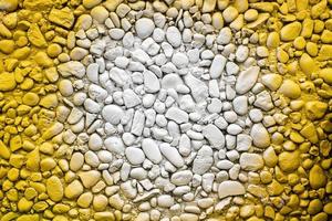 Wall of small stones painted yellow with a white spot in the center. Bright textured background. Copy space. photo