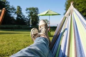 Feet in sneakers and jeans in a hammock, camping, against the backdrop of a summer landscape. photo