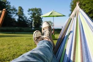 Feet in sneakers and jeans in a hammock, camping, against the backdrop of a summer landscape. photo