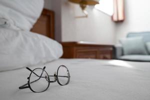 las gafas yacen en la cama, con el telón de fondo de un interior acogedor. foto