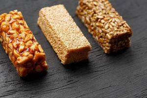 Cereal granola bar with peanuts, sesame and sunflower seeds on a cutting board on a dark stone table. View from above. Three Assorted Bars photo