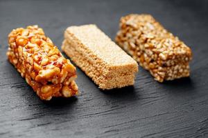 Cereal granola bar with peanuts, sesame and sunflower seeds on a cutting board on a dark stone table. View from above. Three Assorted Bars photo