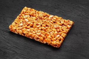 A large golden tile of peanuts, a bar in a sweet molasses on a black texture background. Kozinaki useful and tasty sweets of the East photo