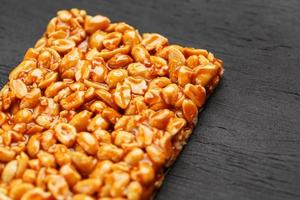 A large golden tile of peanuts, a bar in a sweet molasses on a black texture background. Kozinaki useful and tasty sweets of the East photo