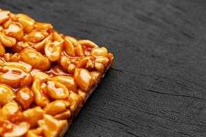 A large golden tile of peanuts, a bar in a sweet molasses on a black texture background. Kozinaki useful and tasty sweets of the East photo