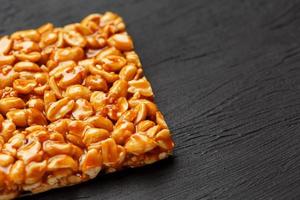 A large golden tile of peanuts, a bar in a sweet molasses on a black texture background. Kozinaki useful and tasty sweets of the East photo