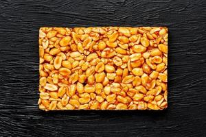 A large golden tile of peanuts, a bar in a sweet molasses on a black texture background. Kozinaki useful and tasty sweets of the East photo