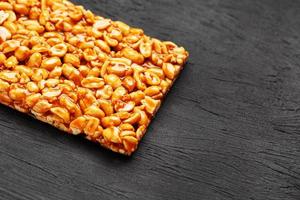 A large golden tile of peanuts, a bar in a sweet molasses on a black texture background. Kozinaki useful and tasty sweets of the East photo