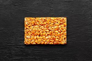 A large golden tile of peanuts, a bar in a sweet molasses on a black texture background. Kozinaki useful and tasty sweets of the East photo