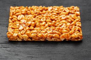 A large golden tile of peanuts, a bar in a sweet molasses on a black texture background. Kozinaki useful and tasty sweets of the East photo