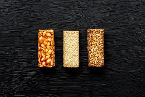 Cereal granola bar with peanuts, sesame and sunflower seeds on a cutting board on a dark stone table. View from above. Three Assorted Bars photo