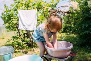 Little preschool girl helps with laundry. Child washes clothes in garden photo