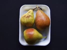 Red and green pears on a black background. Pears in a package from the store. Beautiful fruits of pears. photo