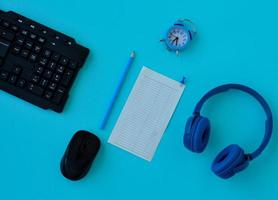 Flat lay home office desk. Workspace with laptop, headphones, pencil, alarm clock and a piece of paper for notes on blue background. Top view feminine background. photo