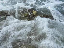 Piedras naturales mojadas cubiertas de musgo y agua de mar y vegetación, las piedras son verdes en un cálido centro turístico del sur del país oriental tropical. fondo, textura foto