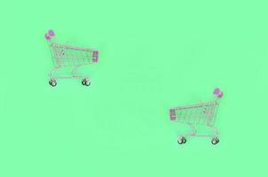 Shopping addiction, shopping lover or shopaholic concept. Small empty shopping cart lies on a pastel colored paper background. Flat lay minimal composition, top view photo
